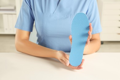 Photo of Female orthopedist showing insole at table in hospital, closeup