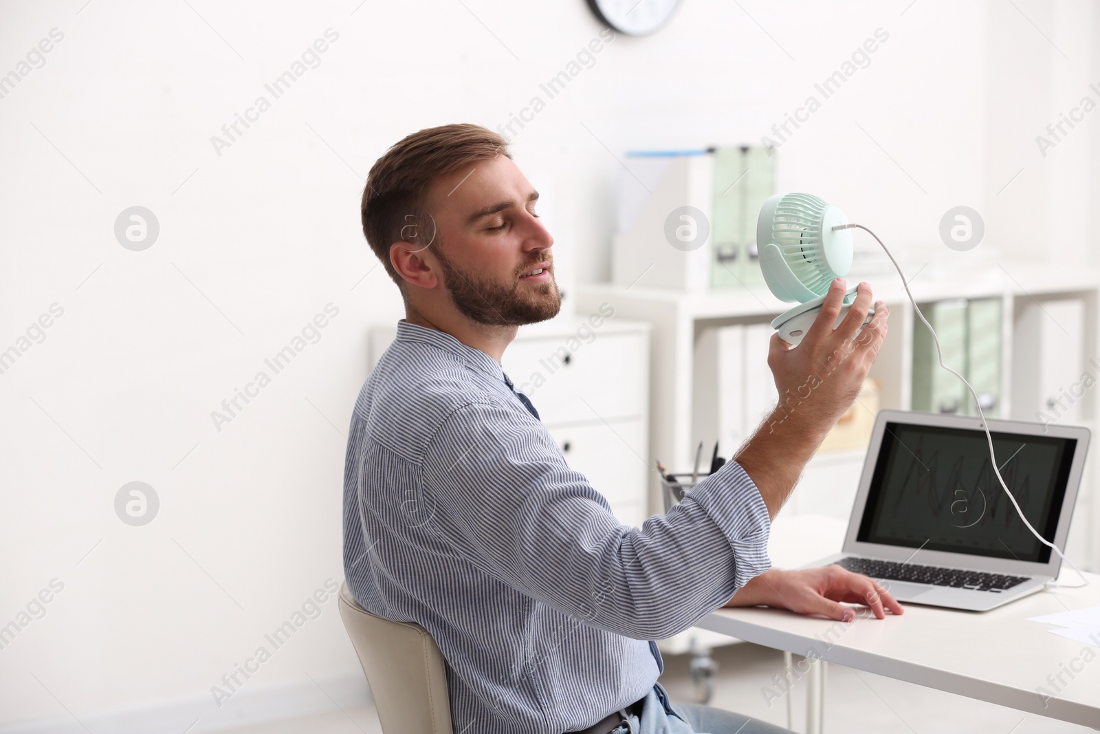 Photo of Man enjoying air flow from fan at workplace