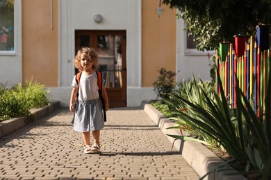 Little girl walking near kindergarten outdoors on sunny day. Space for text