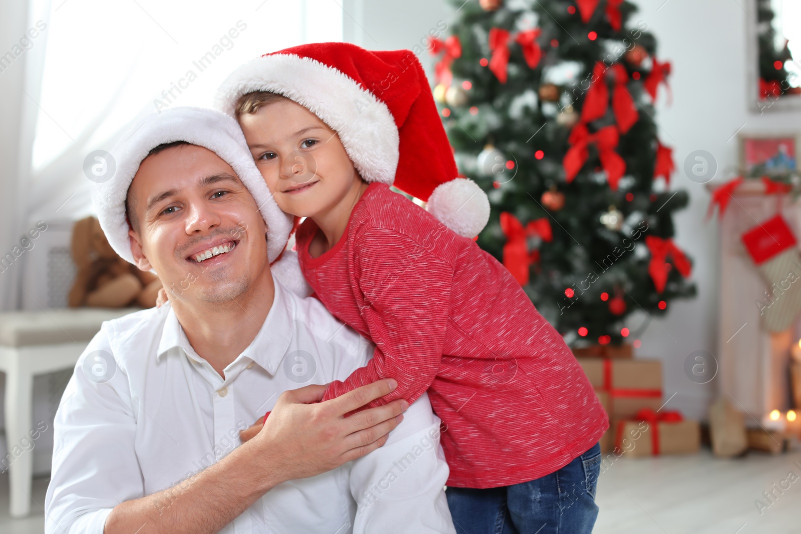 Photo of Father and child in Santa hats celebrating Christmas at home