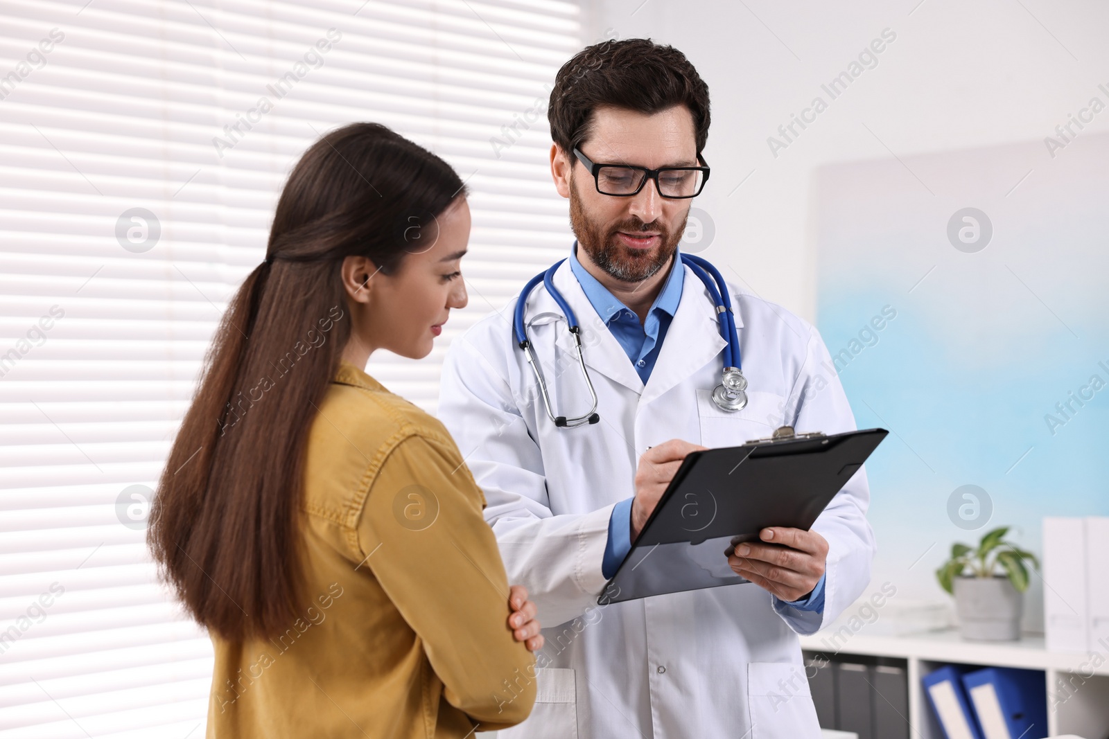 Photo of Doctor with clipboard consulting patient during appointment in clinic