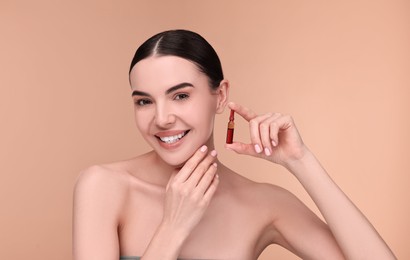 Beautiful young woman holding skincare ampoule on beige background