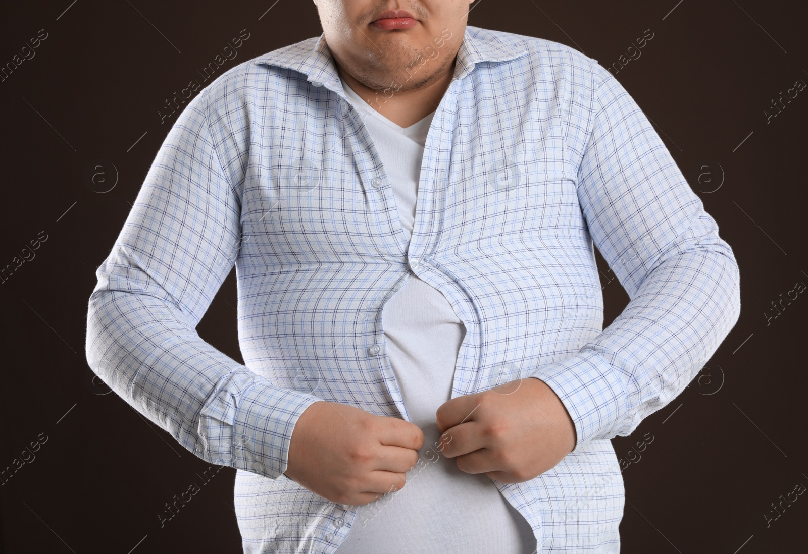 Photo of Overweight man trying to button up tight shirt on dark brown background, closeup