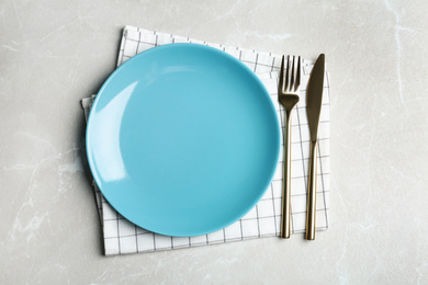 Photo of Empty blue plate with cutlery and napkin on light grey marble table, flat lay