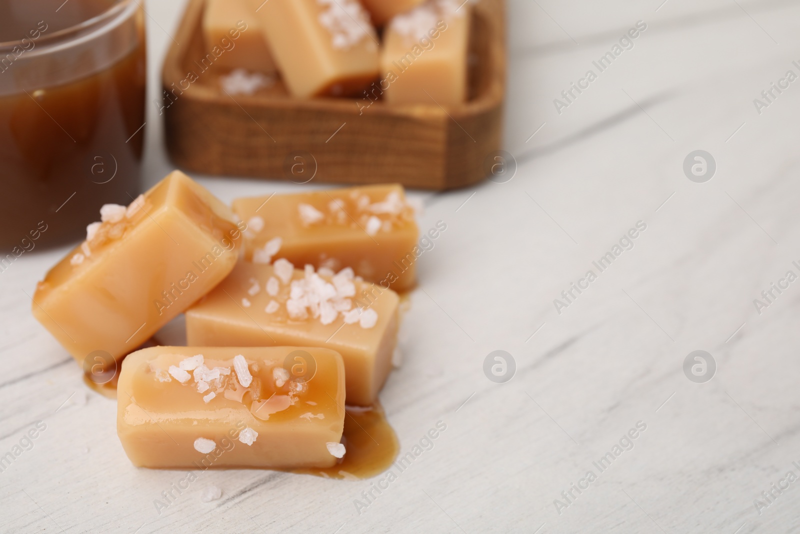 Photo of Yummy caramel candies, sauce and sea salt on white wooden table, closeup. Space for text