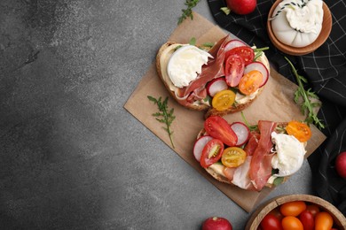 Delicious sandwiches with burrata cheese, ham, radish and tomatoes served on brown textured table, flat lay. Space for text