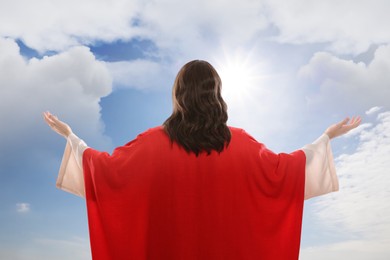 Image of Jesus Christ with outstretched arms against blue sky, back view