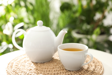 White cup of tea and teapot on table against blurred background