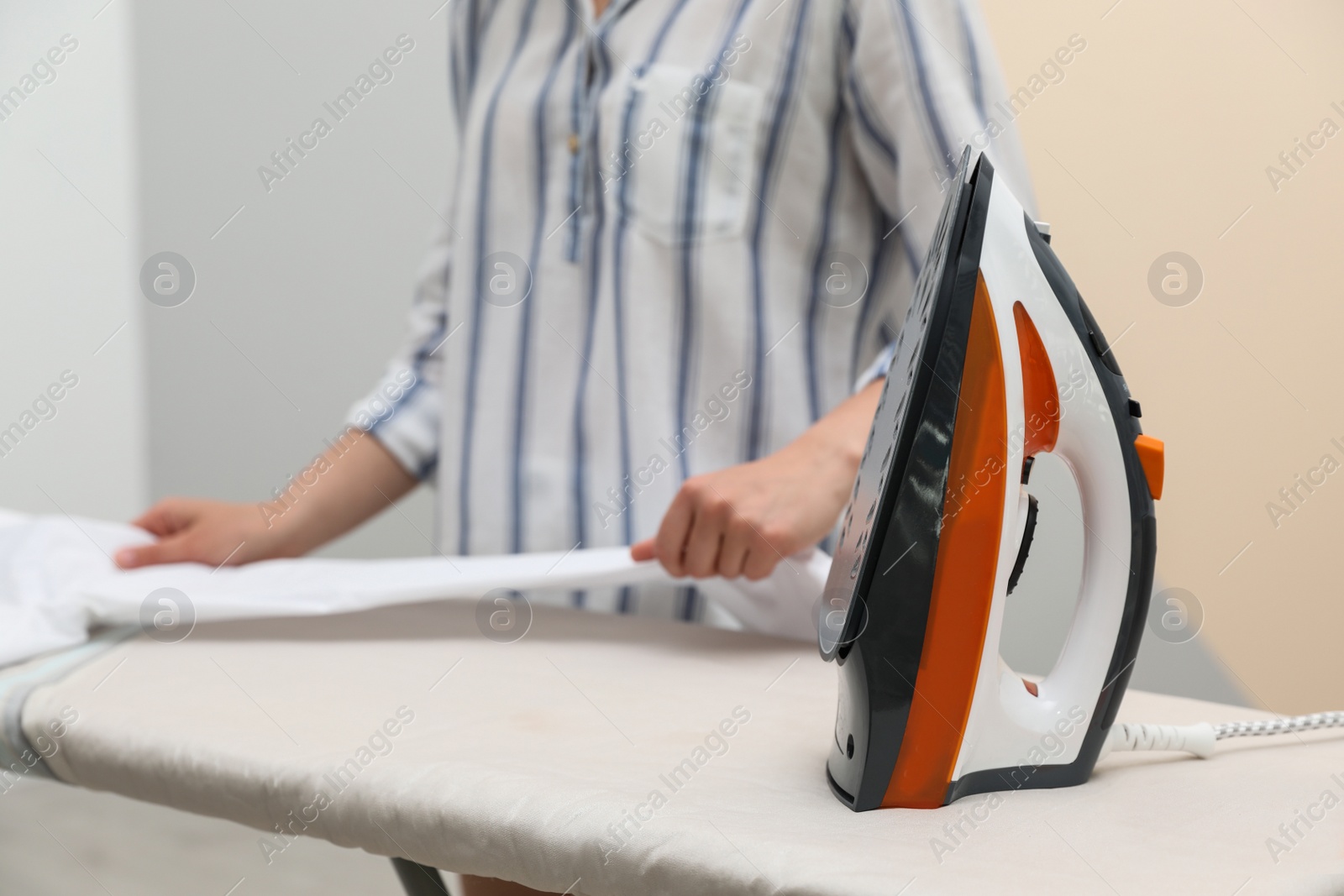 Photo of Woman ironing clean shirt on board against color background, closeup with space for text. Laundry day