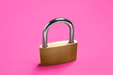 Photo of One locked steel padlock on pink background, closeup