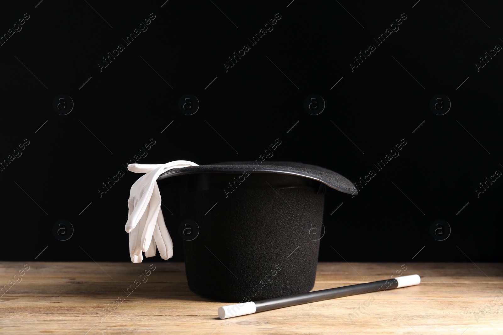 Photo of Magician's hat, gloves and wand on wooden table against black background