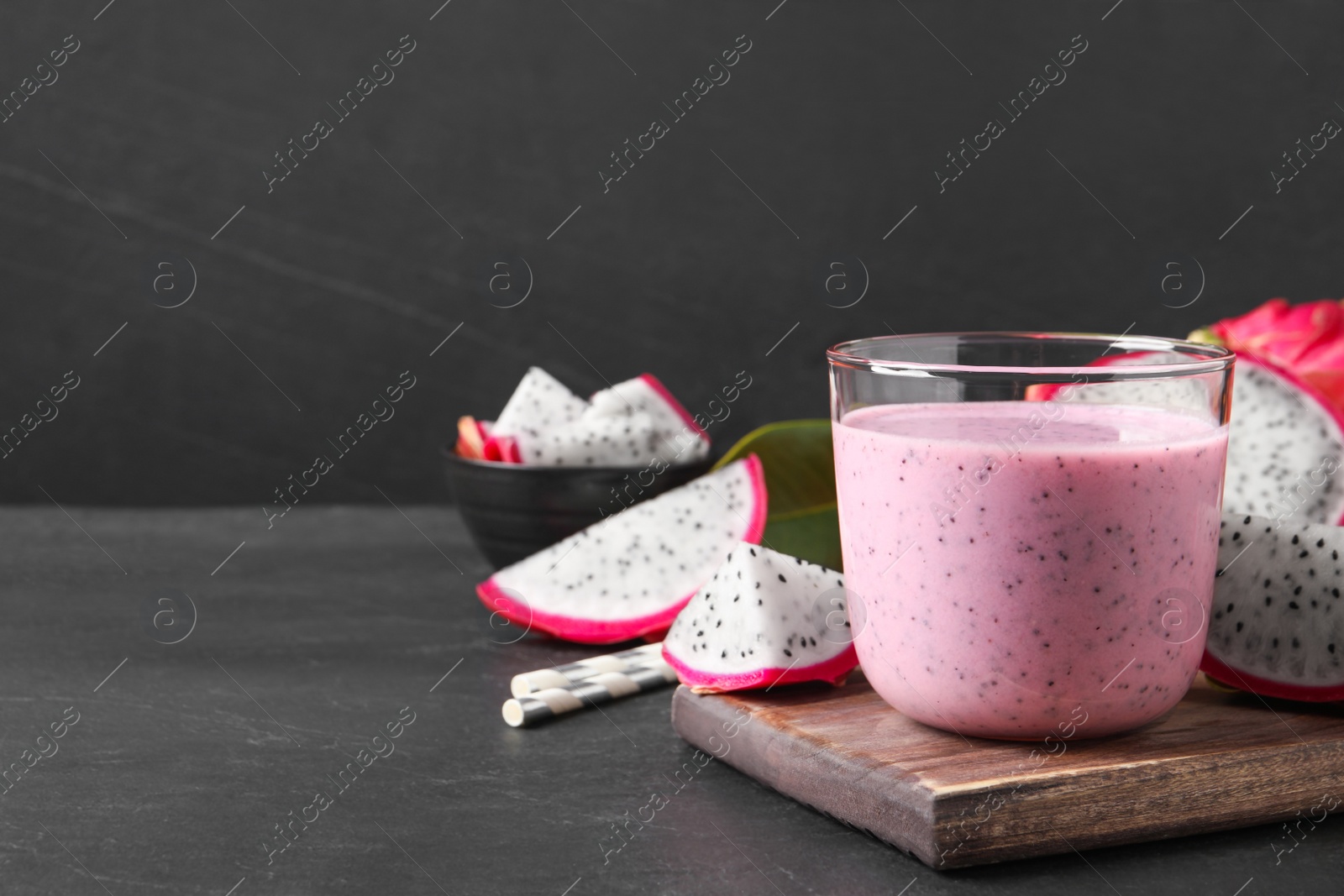Photo of Delicious pitahaya smoothie and fresh fruits on black table, space for text
