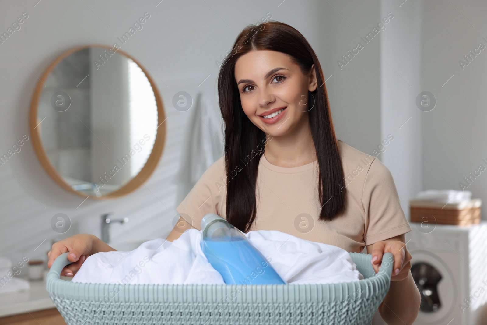 Photo of Woman holding basket with dirty clothes and fabric softener in bathroom