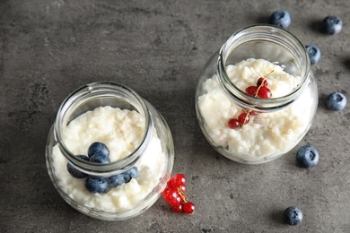 Photo of Creamy rice pudding with red currant and blueberries in jars on grey background