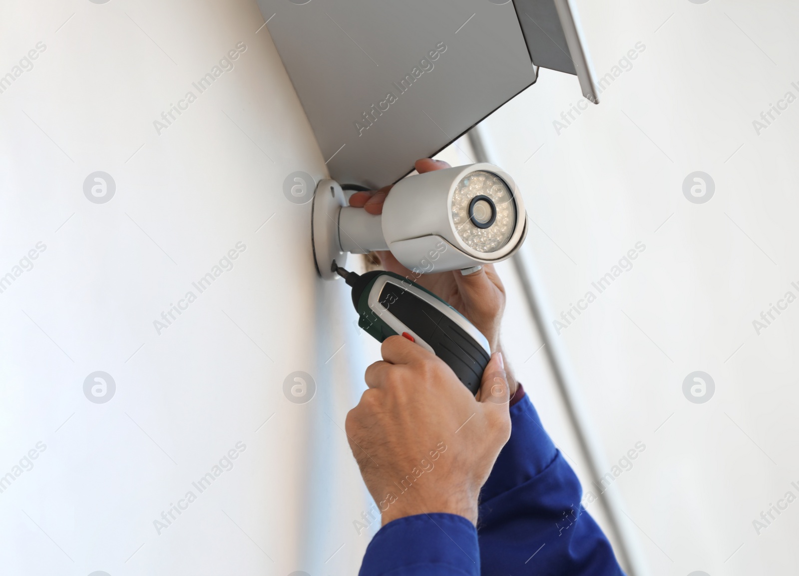 Photo of Technician installing CCTV camera on wall outdoors, closeup
