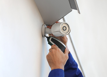 Photo of Technician installing CCTV camera on wall outdoors, closeup