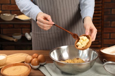 Photo of Cooking chocolate chip cookies. Woman adding butter to dough at wooden table in kitchen, closeup