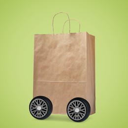 Image of Paper shopping bag on wheels against yellowish green background. Delivery service
