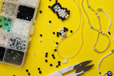Photo of Beautiful handmade beaded jewelry, crafts and supplies on yellow background, flat lay