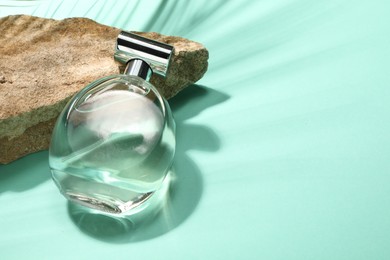 Bottle of luxury perfume in sunlight and stone on turquoise background, space for text