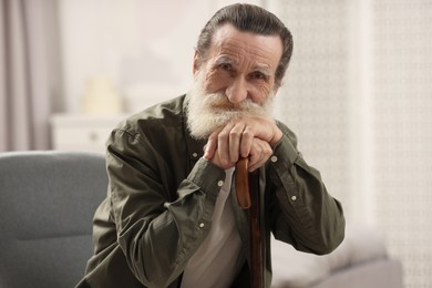 Photo of Senior man with walking cane on chair at home