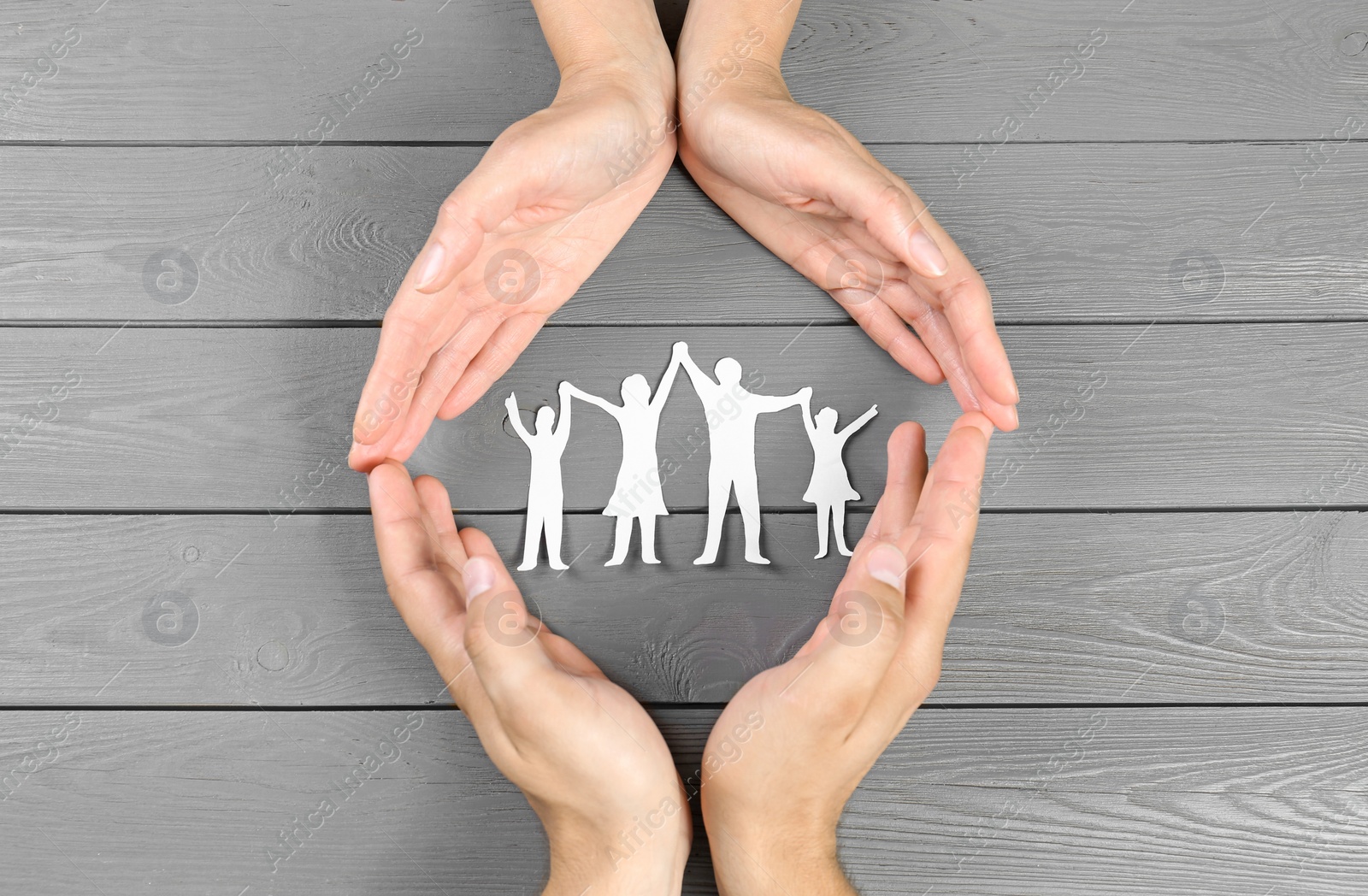 Photo of Young man and woman protecting paper family figure with their hands on grey wooden background, top view