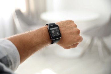Image of Young man showing electronic wristwatch with Smart Home Interface indoors, closeup