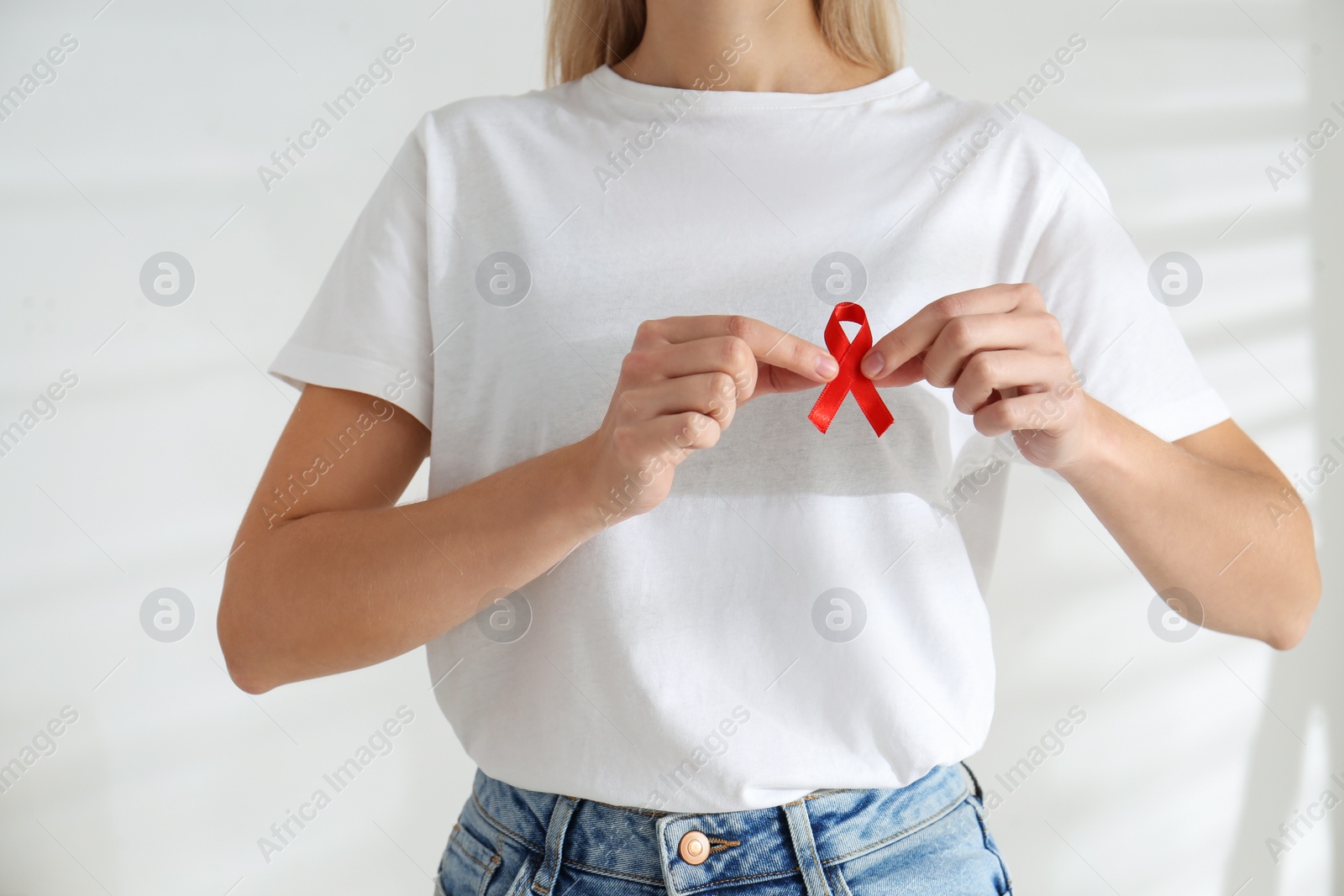 Photo of Woman holding red awareness ribbon on light background, closeup. World AIDS disease day