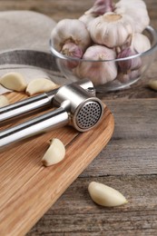 Photo of Garlic press and cloves on wooden table. Kitchen utensil