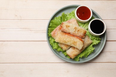 Photo of Delicious fried spring rolls and sauces on light wooden table, top view. Space for text