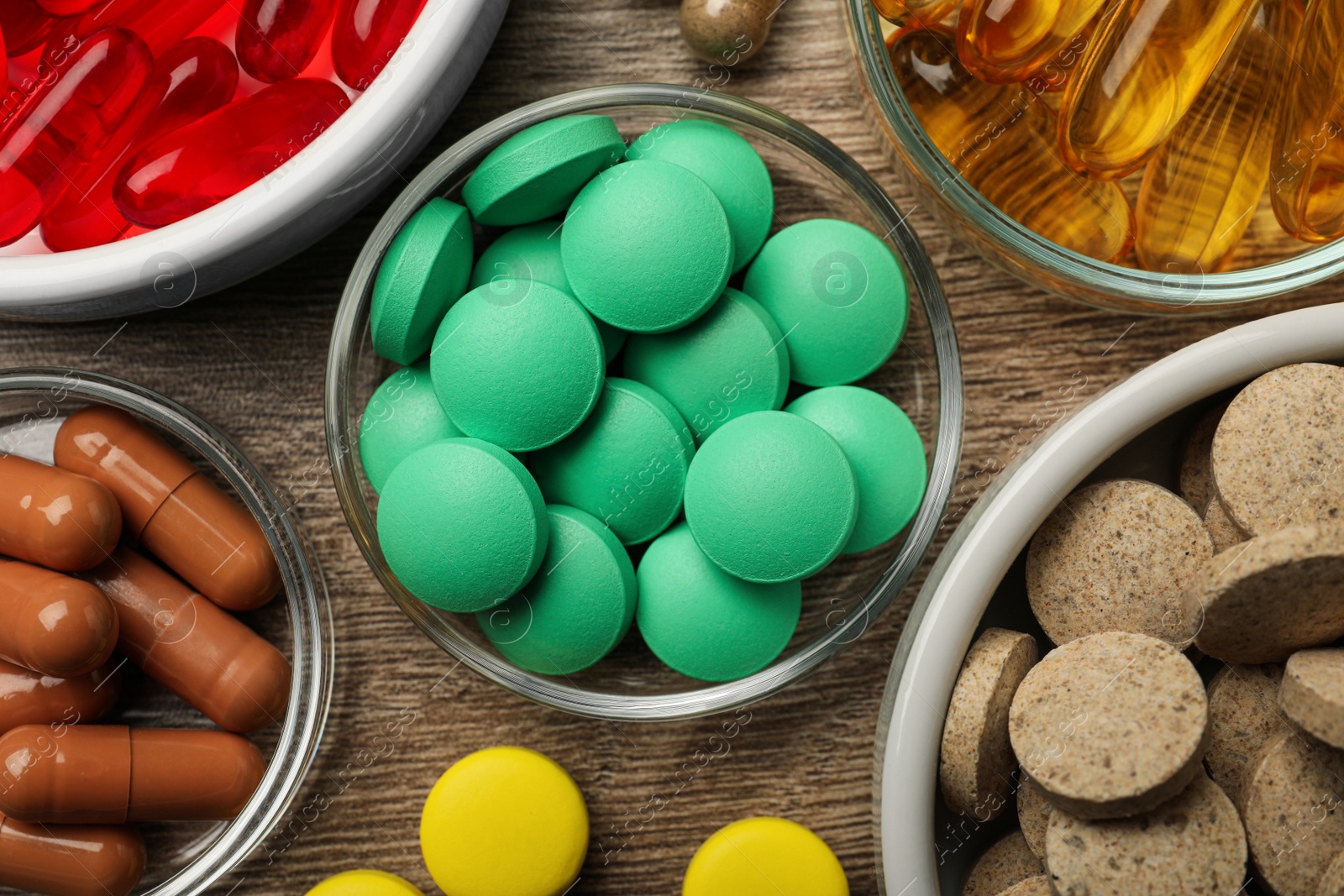 Photo of Different dietary supplements in bowls on wooden table, flat lay