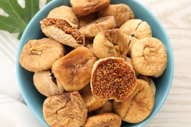 Photo of Bowl with tasty dried figs and green leaf on white wooden table, top view