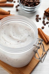Body scrub in glass jar, cinnamon and coffee beans on white wooden table, closeup