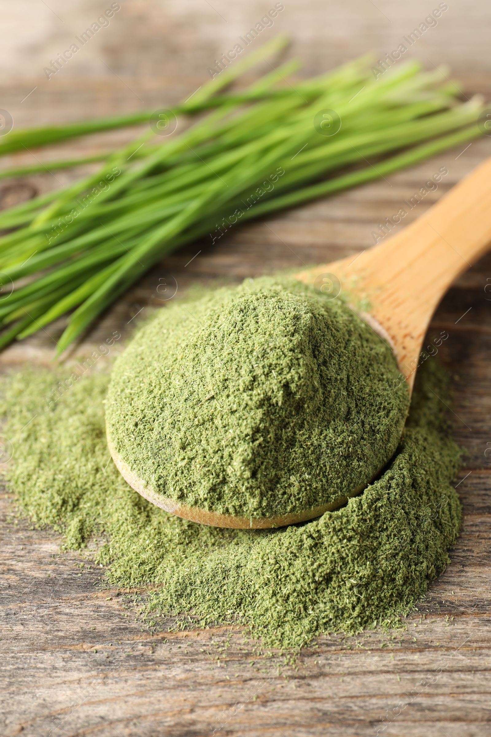 Photo of Wheat grass powder in spoon on wooden table, closeup