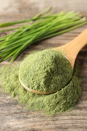 Photo of Wheat grass powder in spoon on wooden table, closeup