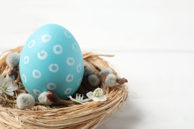 Photo of Colorful Easter egg in decorative nest on white wooden table, closeup. Space for text