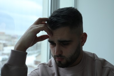 Photo of Portrait of sad man near window at home