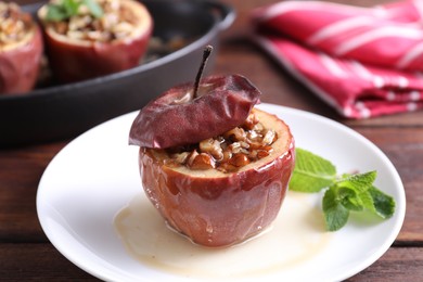 Photo of Tasty baked apple with nuts, honey and mint on wooden table, closeup