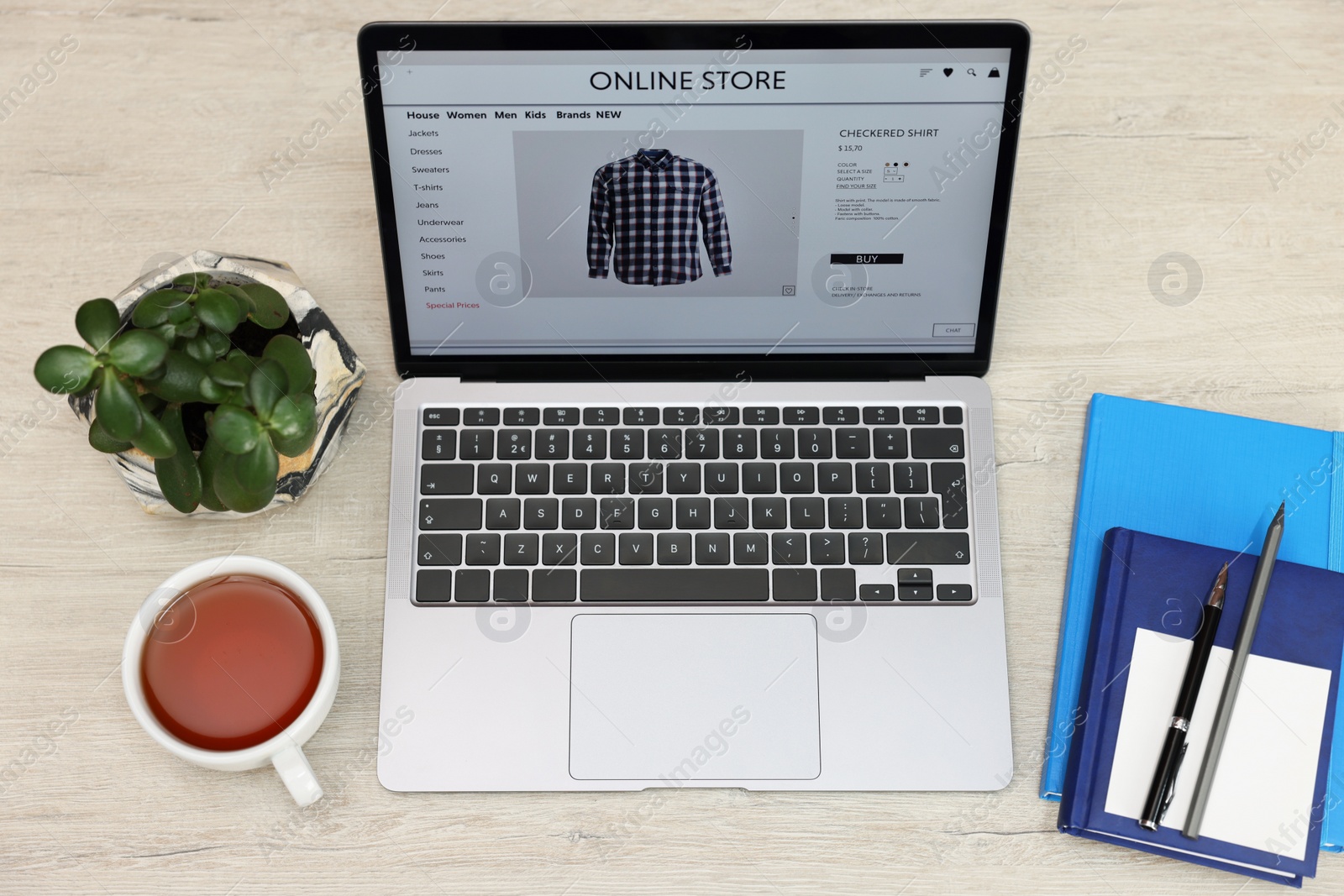 Photo of Online store. Laptop with open website, notebooks, pen and pencil on wooden table, above view