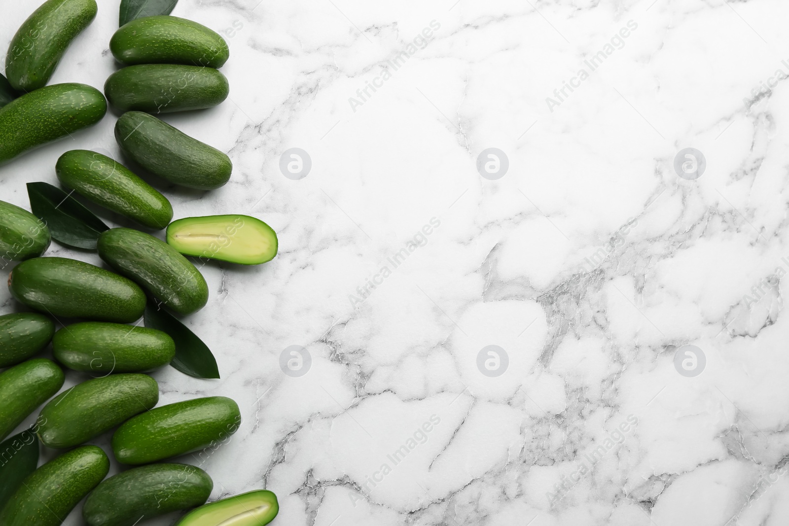 Photo of Fresh seedless avocados with green leaves on marble table, flat lay. Space for text