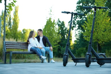 Photo of Modern electric kick scooters and couple spending time together in park, selective focus