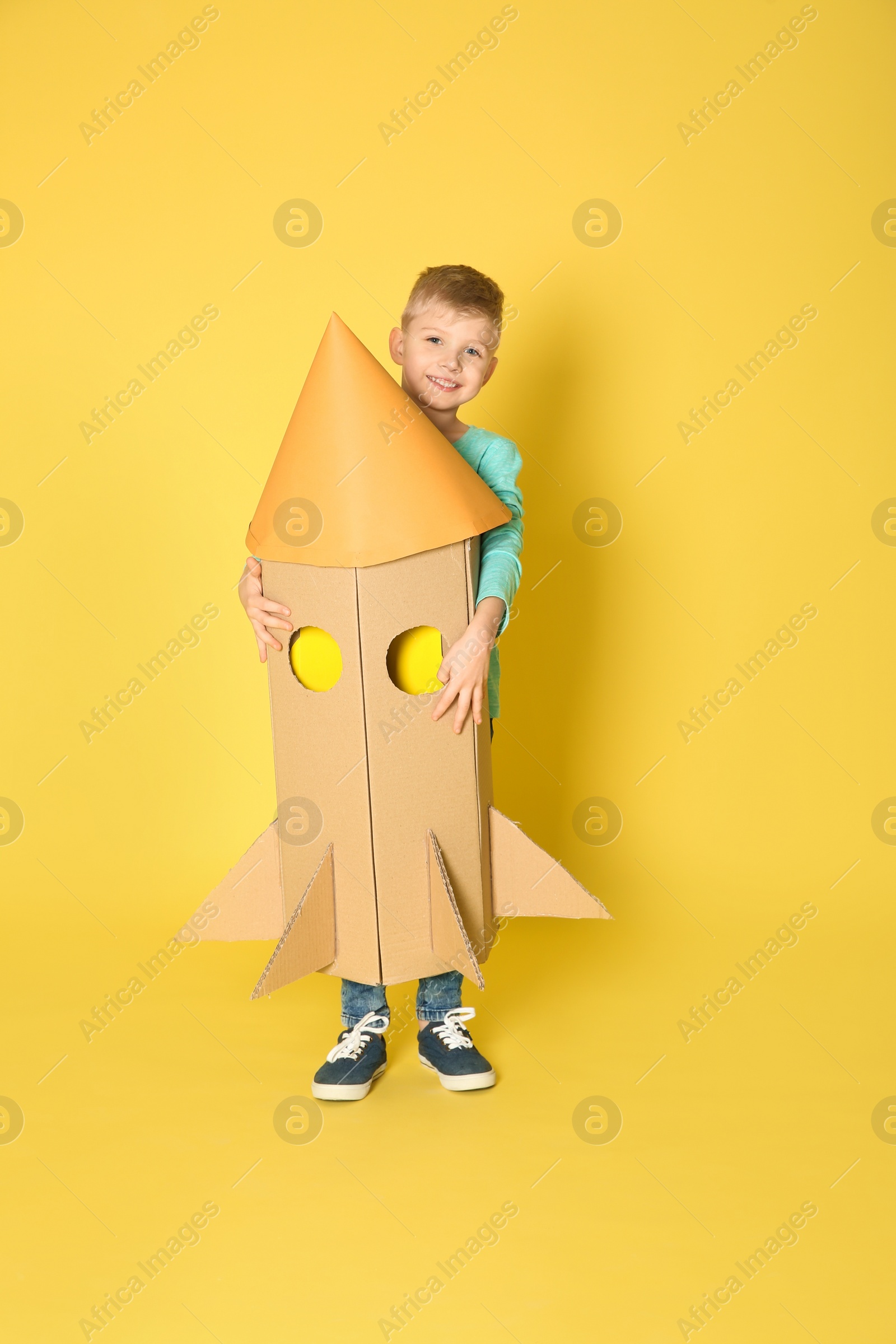 Photo of Little child playing with rocket made of cardboard box on yellow background