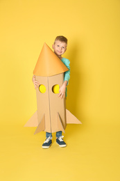 Little child playing with rocket made of cardboard box on yellow background