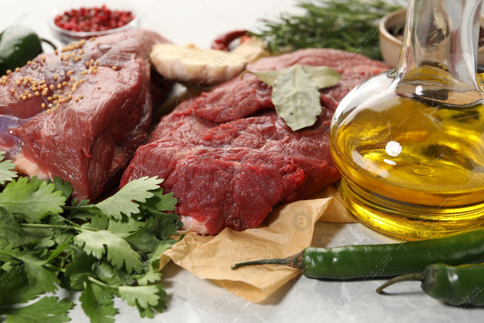 Photo of Pieces of raw beef meat, parsley and spices on light grey marble table, closeup