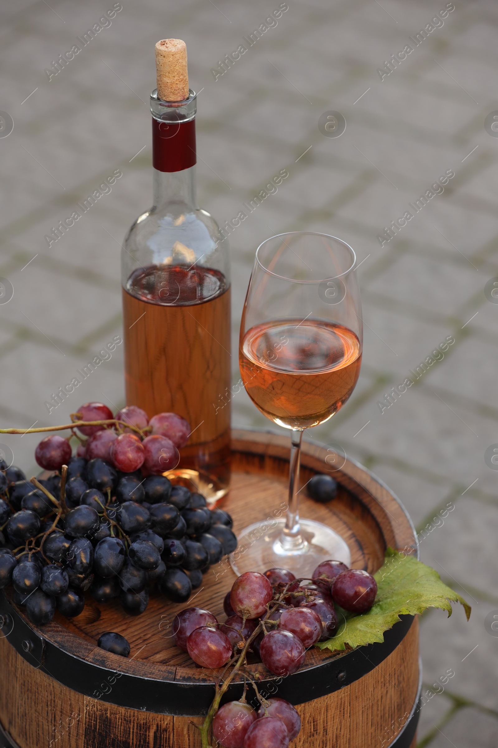 Photo of Delicious wine and ripe grapes on wooden barrel outdoors