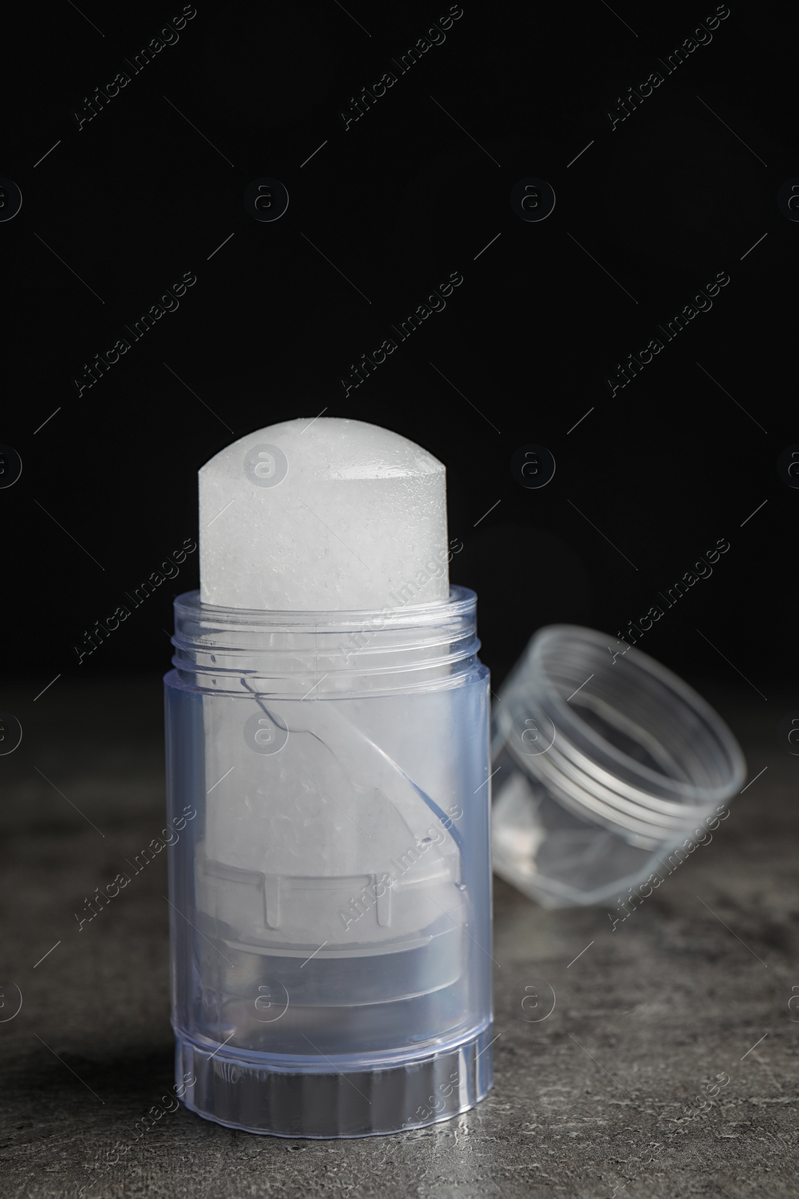 Photo of Natural crystal alum deodorant and cap on grey table against black background