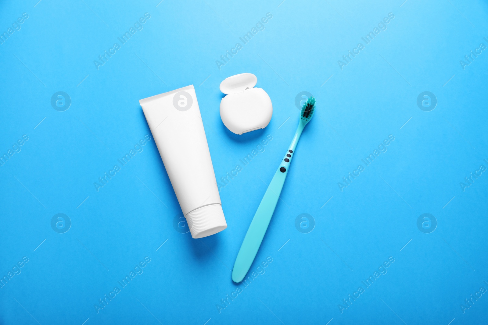 Photo of Container with dental floss, toothpaste and toothbrush on light blue background, flat lay