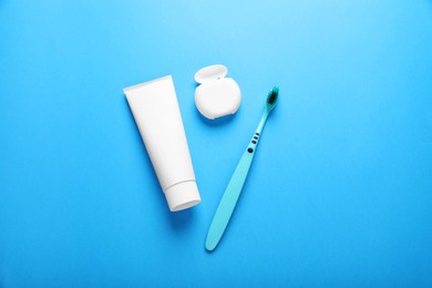 Photo of Container with dental floss, toothpaste and toothbrush on light blue background, flat lay