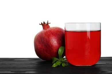 Photo of Refreshing pomegranate juice in glass, leaves and fruit on black wooden table against white background. Space for text