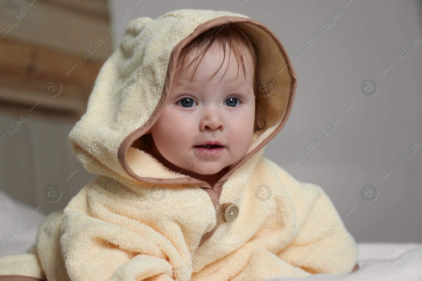 Photo of Cute little baby in yellow hooded towel on bed after bath